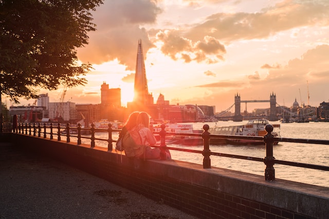 a young couple sit on the banks of the thames watching the sun set