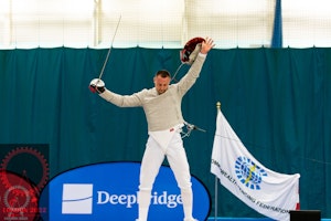 JJ Webb in fencing attire with his arms in the air celebrating his win.