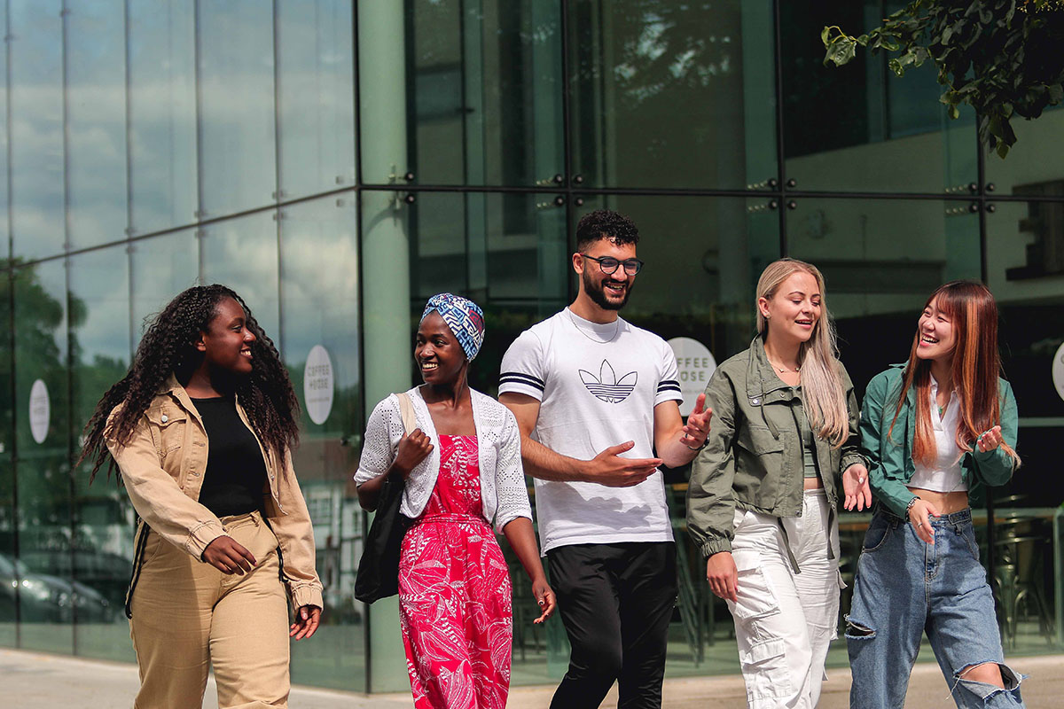 A group of young people walking on the sidewalk, enjoying each other's company and the pleasant weather.