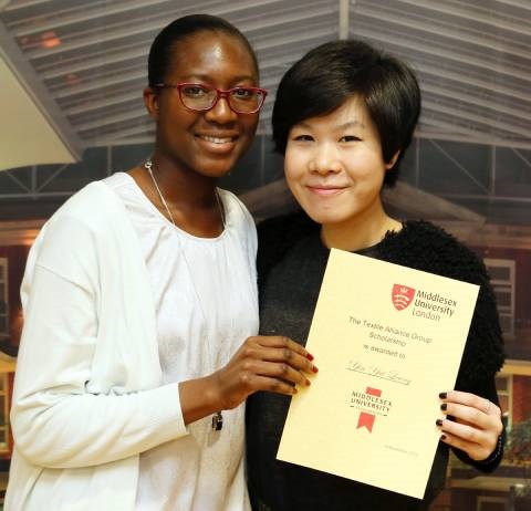 Two women proudly displaying a certificate in front of a building, symbolizing their achievement.