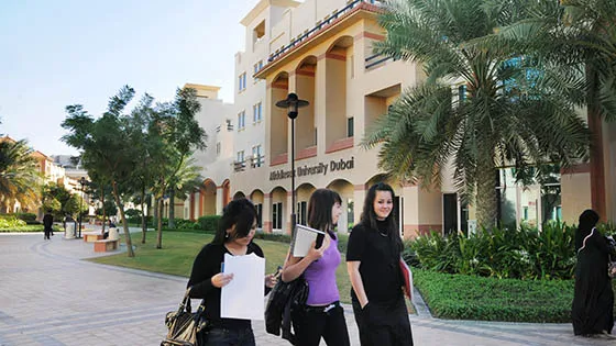 Three young women walking down a sidewalk at Dubai campus Exterior, each carrying books.
