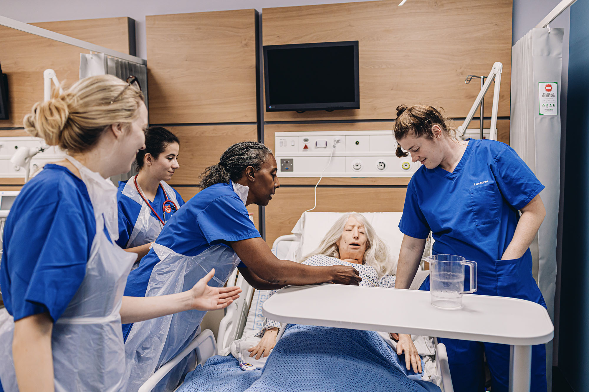 nurse demos procedure with dummy while student nurses watch on