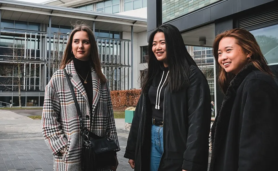 Three young women posing outside a building, smiling and looking confident.