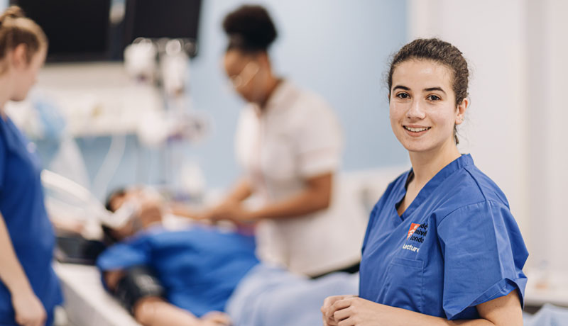 Midwifery student looking at camera with students working in the background.