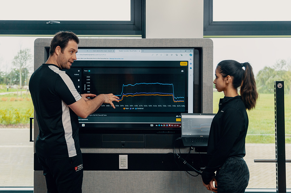 Sport performance student being taught in class, next to a screen filled with analytics